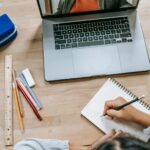 clever schoolgirl doing homework in notebook while having online lesson